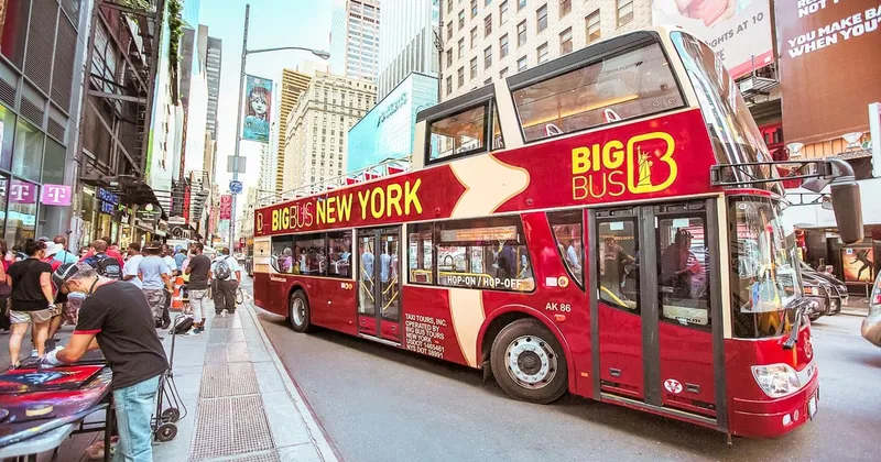 Open-top double-decker on a NYC bus tour passing Times Square at dusk with passengers on the upper deck