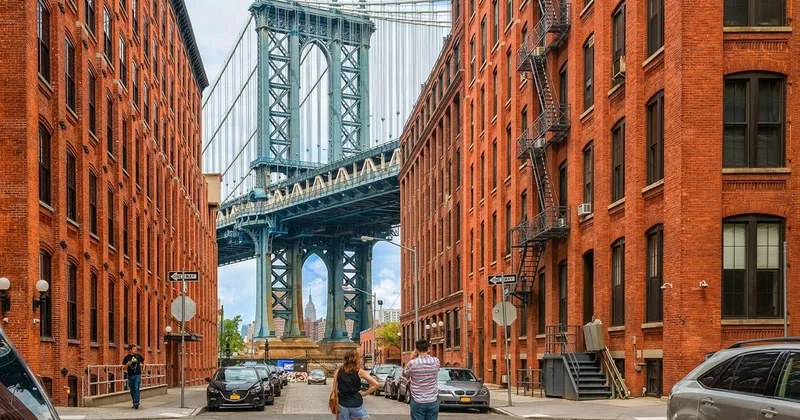 Guide leading visitors on a Brooklyn and DUMBO NYC bus tour with the Manhattan Bridge framing the Empire State Building