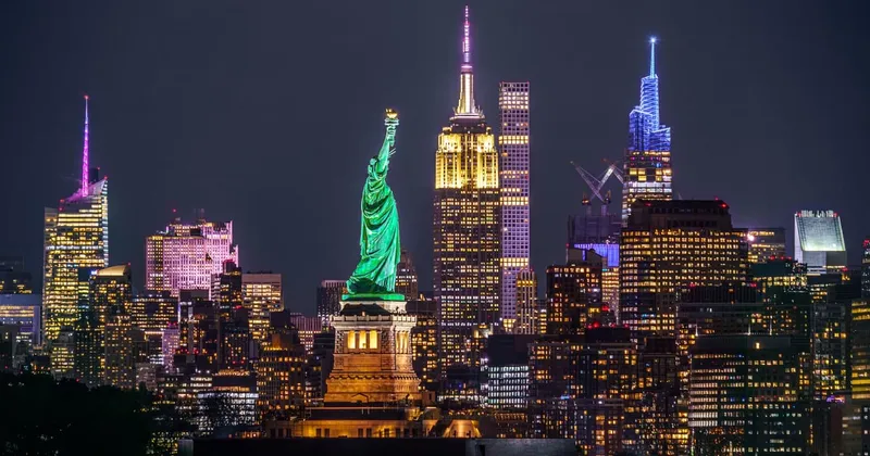 Closed-top luxury coach on a New York bus tour at night with the Manhattan skyline lit behind the Brooklyn Bridge