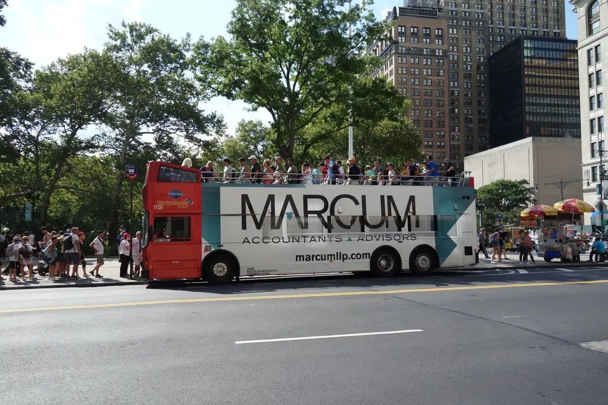A red open-top double-decker sightseeing bus at State Street and Battery Place on a NYC hop-on hop-off bus tour